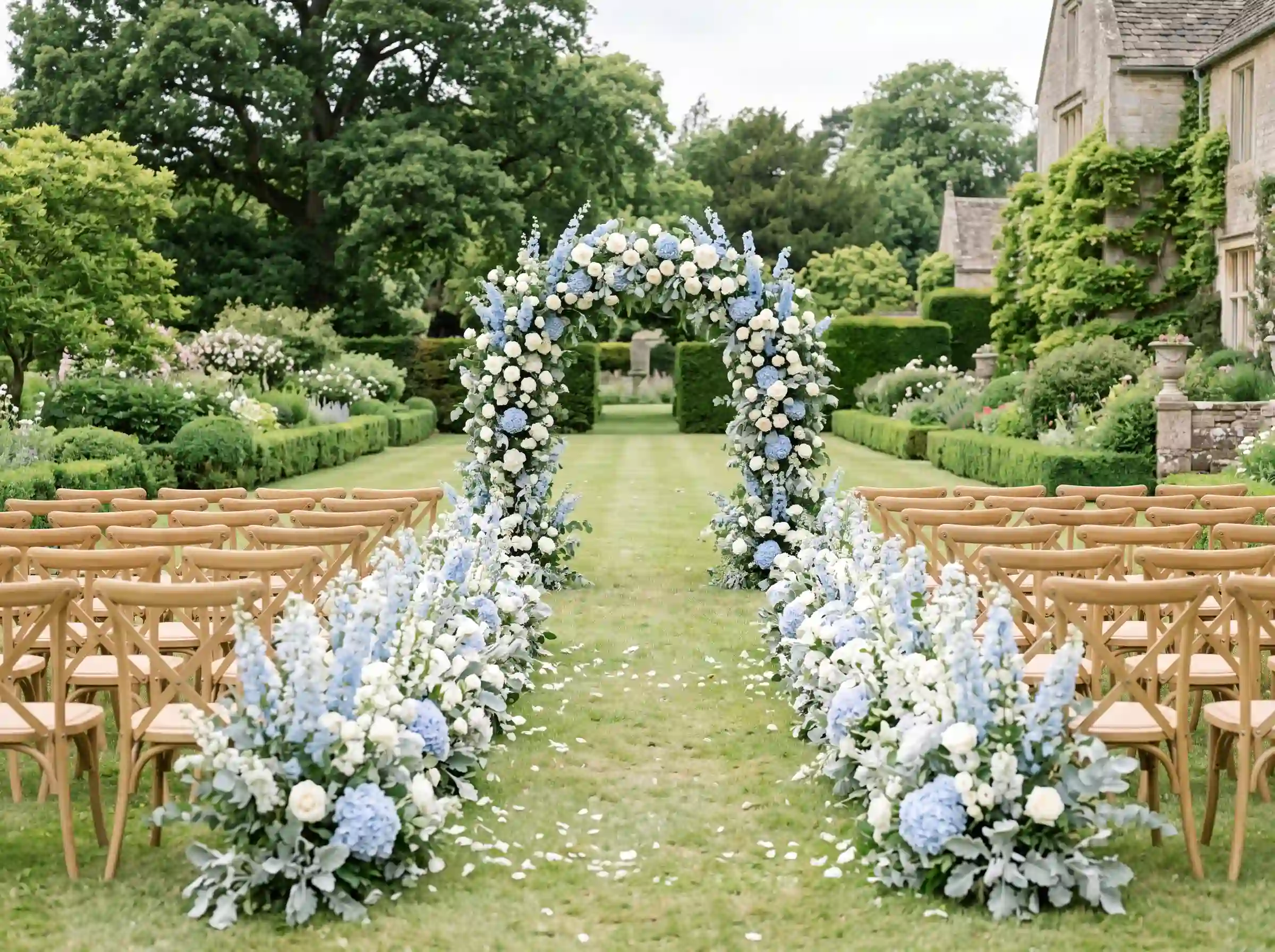 Manor garden wedding ceremony with dusty blue hydrangea floral arch and wooden crossback chairs