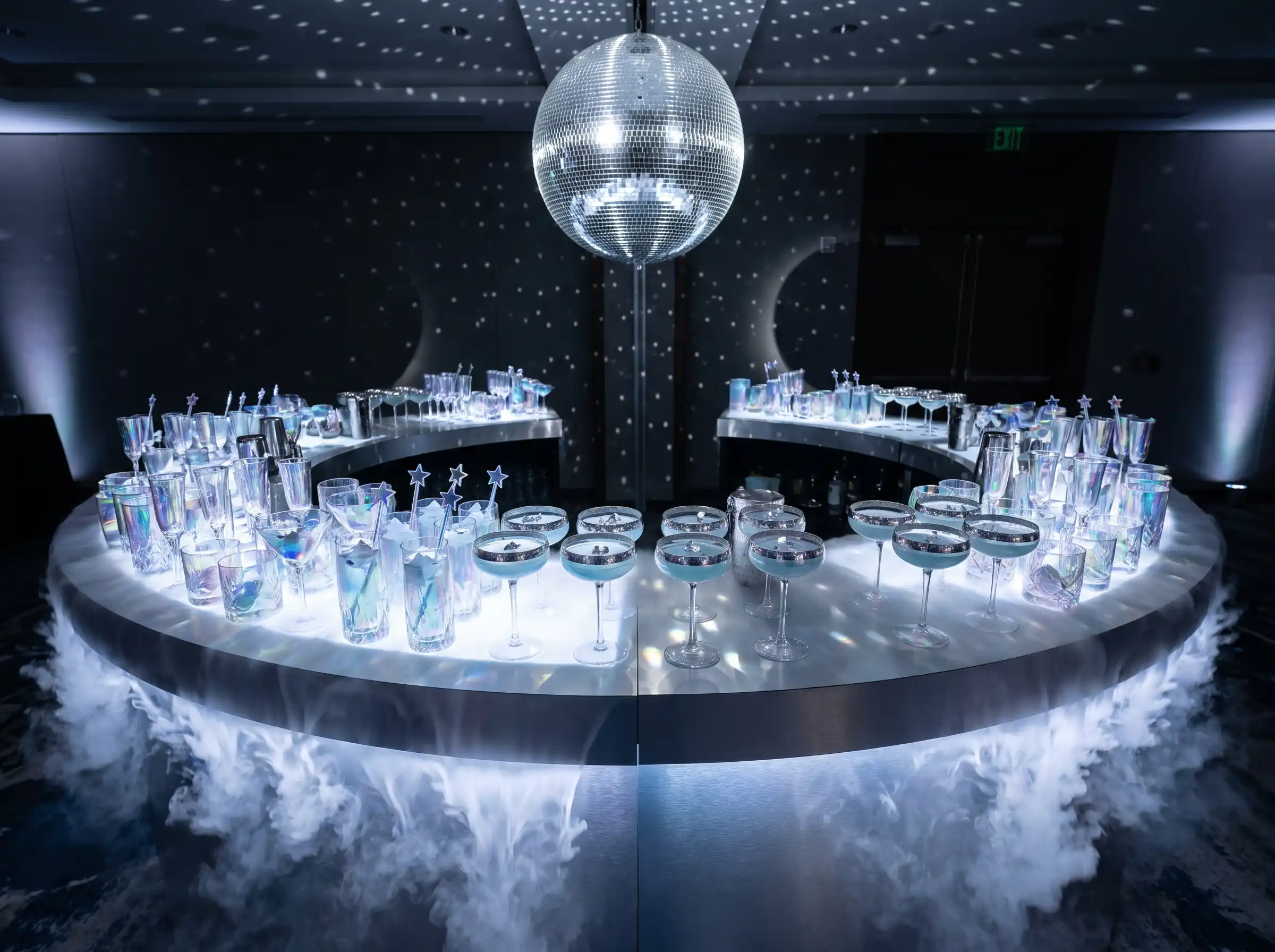 Crescent shaped cocktail bar with iridescent glassware pale blue cocktails dry ice fog and suspended disco ball