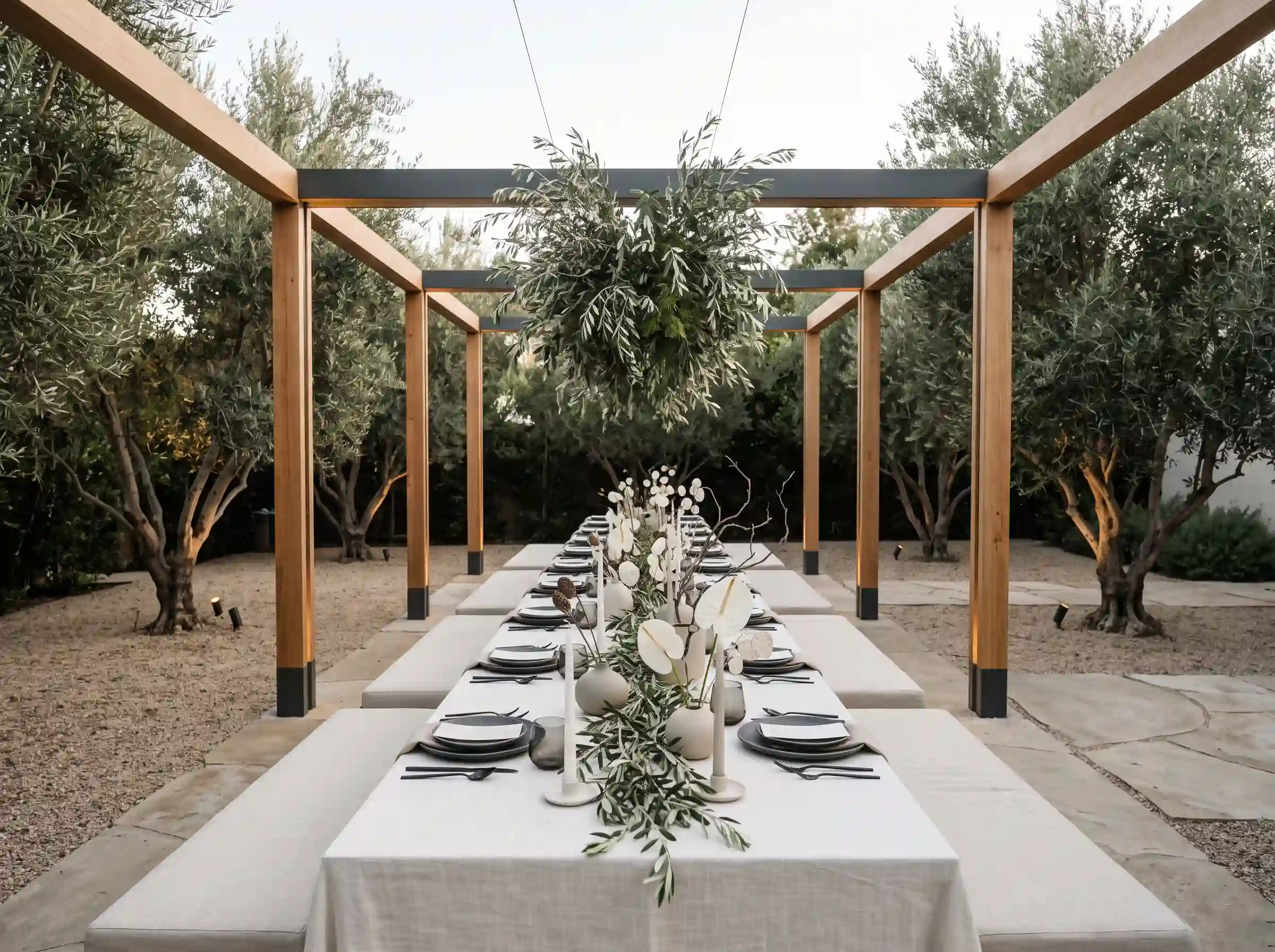 Minimalist olive grove reception with single long table clean pergola frame and sculptural branch centerpieces