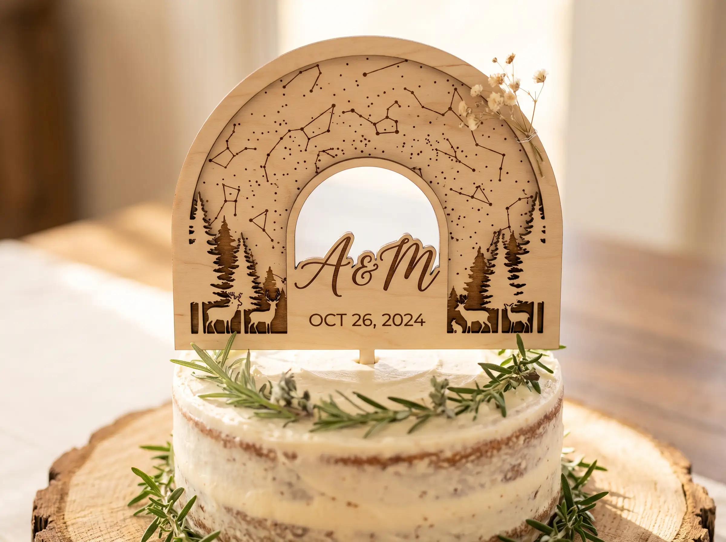 Laser-cut wooden arch cake topper with constellations pine trees deer initials and date on naked cake