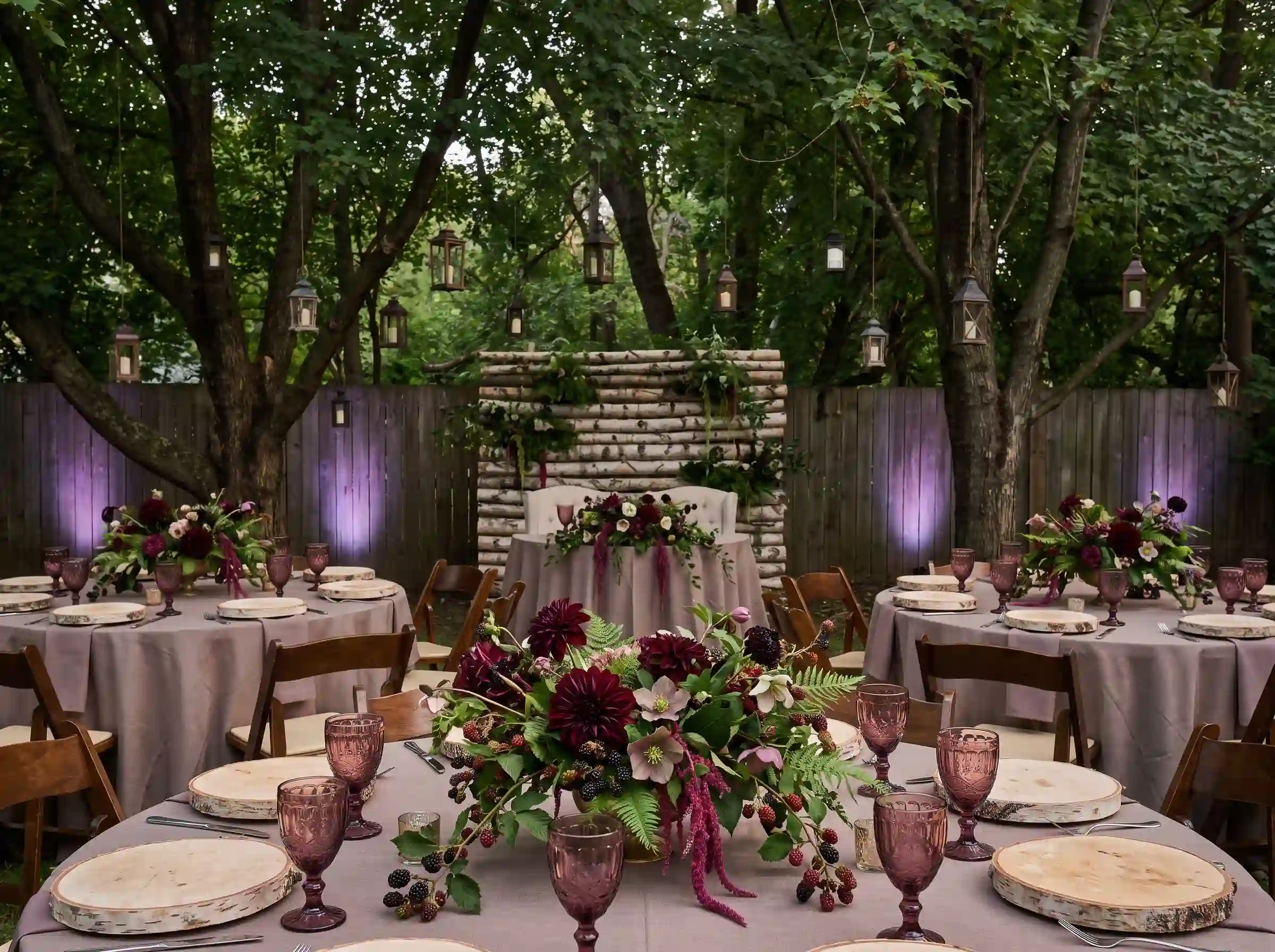 Moody forest-inspired evening reception with blackberry florals, birch bark chargers, and violet uplighting