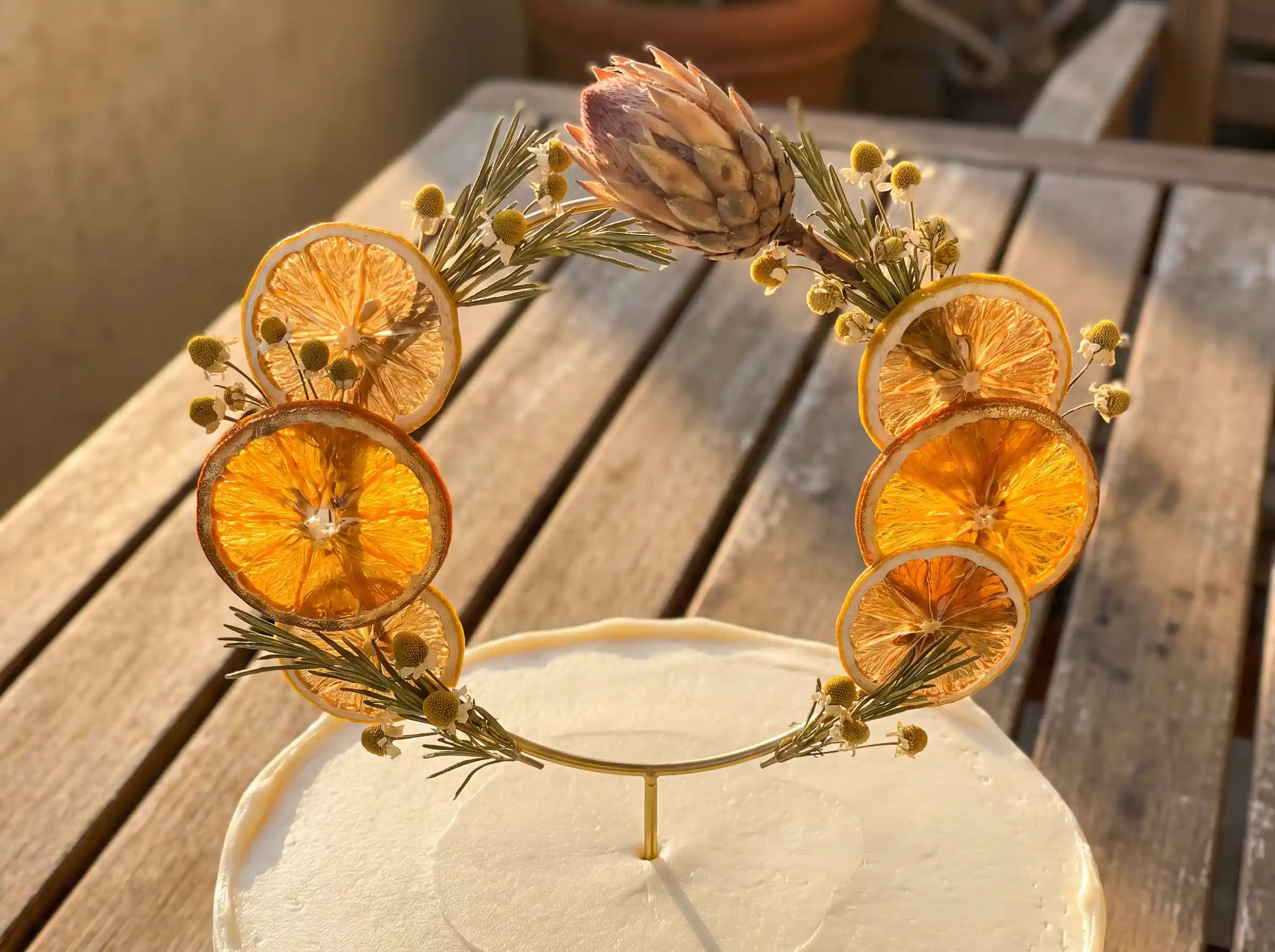 Dried orange slice halo cake topper with protea chamomile and rosemary on white cake outdoors