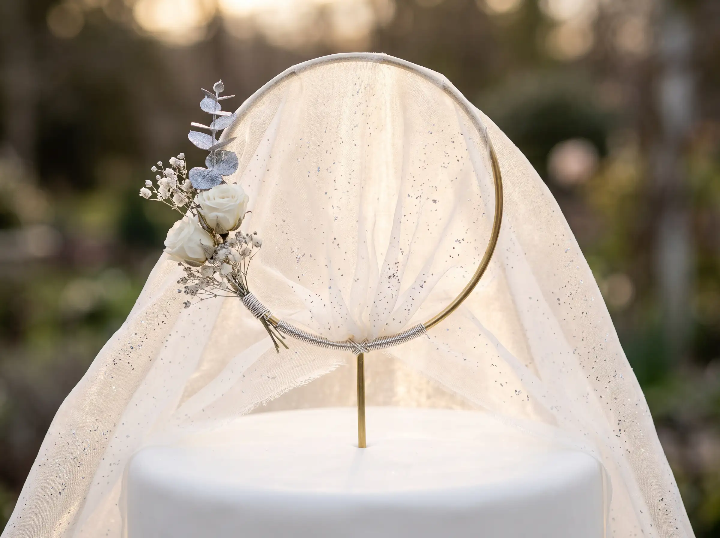 Gold hoop cake topper draped with glittering tulle veil roses and eucalyptus on white cake