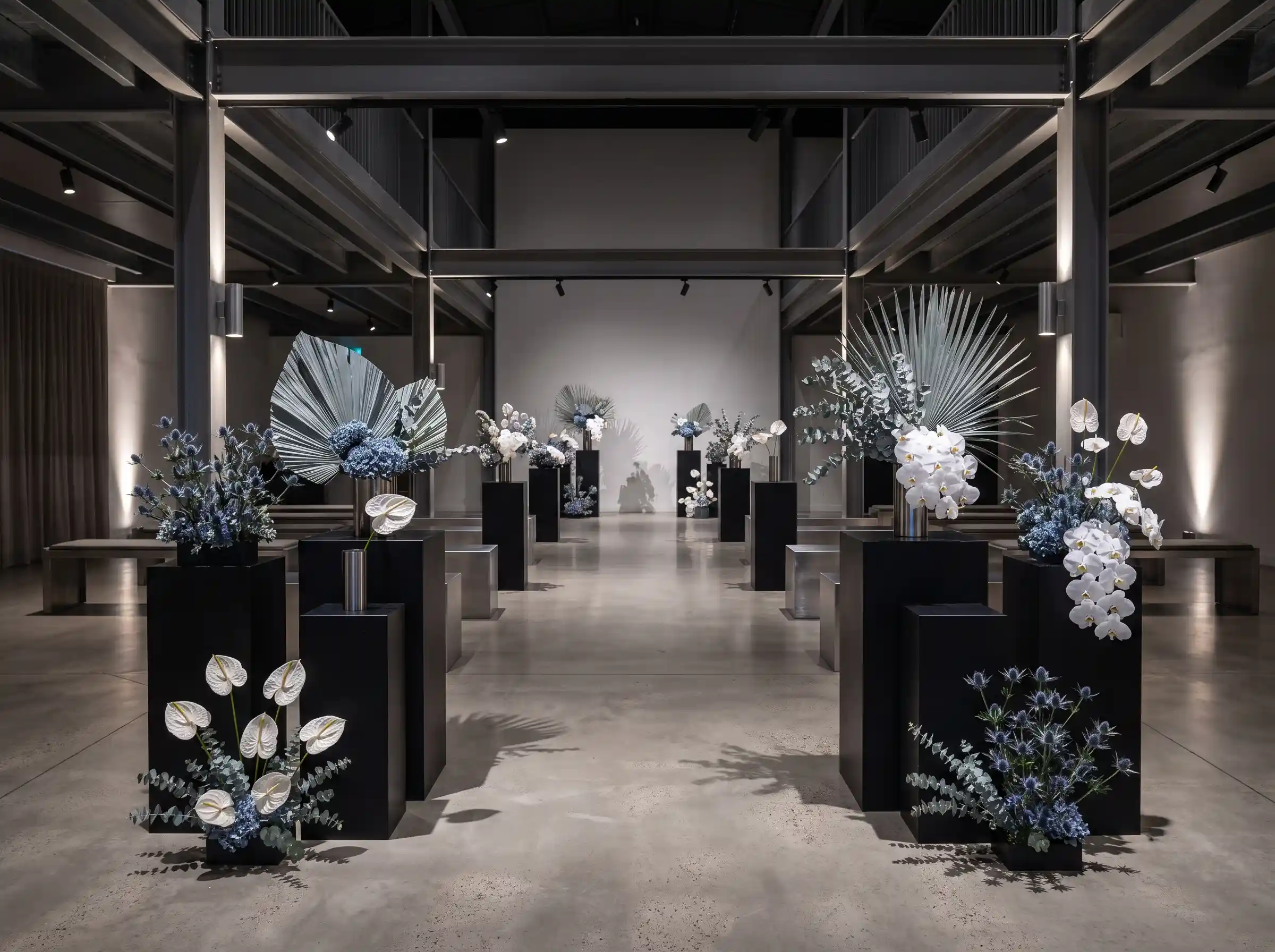Sculptural blue eryngium with white anthuriums and orchids on matte black plinths in a contemporary wedding display