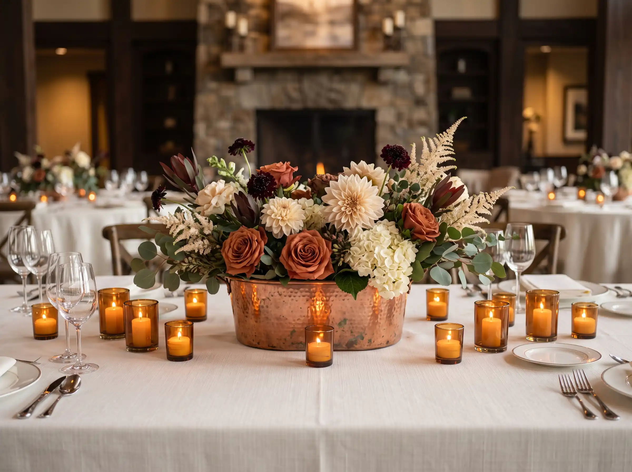 copper vessels holding warm toned garden flowers on a rustic wedding reception table